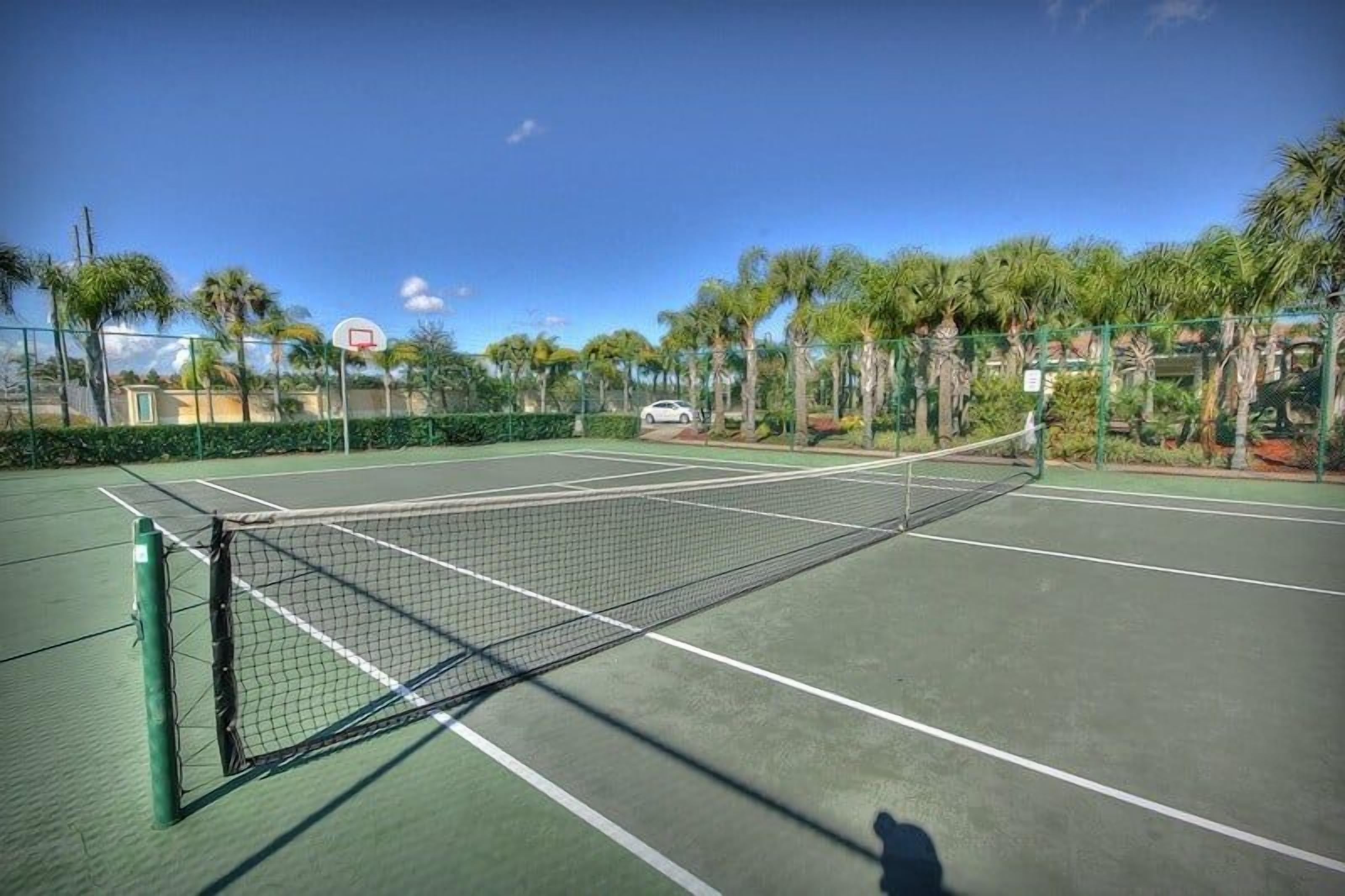 Ein Tennisplatz im Freien mit Netz, umgeben von einem Zaun und Palmen.