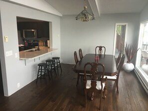 A dining area with a wooden table and chairs, a kitchen area with a microwave and cabinets, and a large window providing natural light.