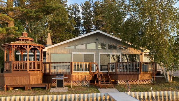 A wooden cabin with a deck, a small gazebo, and a dock extending into a body of water. - Large Lake House 30 Feet From The Water With Private Dock Out The Door.  (Mears)