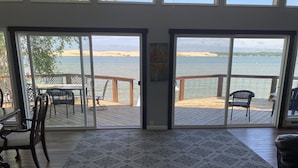 A room with a large sliding glass door leading to a wooden deck overlooking a body of water. - Large Lake House 30 Feet From The Water With Private Dock Out The Door.  (Mears)