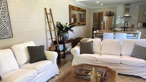 Een woonkamer met witte banken, een geweven salontafel, een ladder en een potplant.