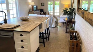 Een keuken met een houten aanrechtblad, witte kastjes en een groot eiland. Er is een eethoek met witte stoelen en een tafel.