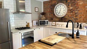 Een keuken met witte kasten, een roestvrijstalen afzuigkap, een magnetron, een klok en een houten aanrecht.
