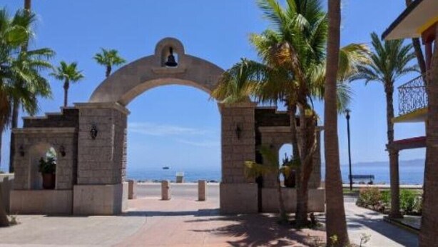 Una entrada arqueada con una campana, palmeras y una vista despejada del océano.