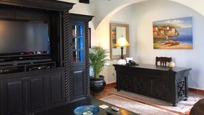 Una sala de estar con un mueble de madera oscura, un televisor de pantalla plana, una lámpara, un cuadro y una planta en maceta.