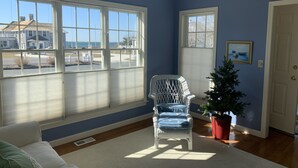A room with large windows, a wicker chair, a small Christmas tree, and a white door. - Bright & Airy 3BR Home with Views of Lewis Bay! (1498) (West Yarmouth)