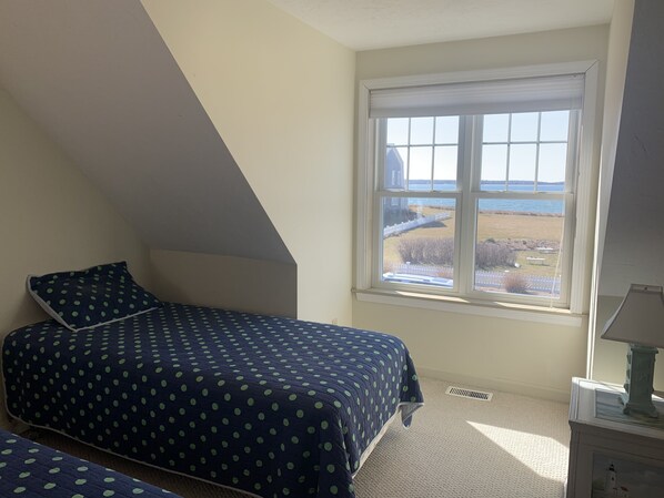 Un dormitorio con cama, ventana con vista al mar y lámpara en una mesita de noche.