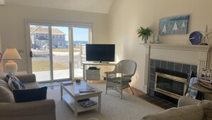 A living room with a television, a fireplace, and a view of the outside. - Bright & Airy 3BR Home with Views of Lewis Bay! (1498) (West Yarmouth)