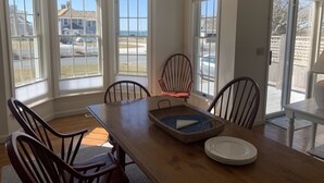 A dining area with a wooden table, four chairs, a basket, and a set of plates. - Bright & Airy 3BR Home with Views of Lewis Bay! (1498) (West Yarmouth)