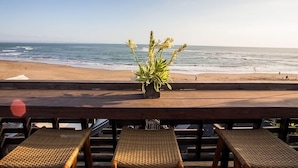 A beach view with a wooden deck, wicker lounge chairs, and a potted plant. - 5 Bedroom villa Beachfront with private Pool in Canggu (Canggu)