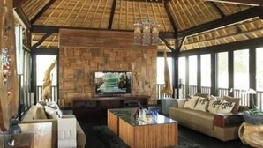 A spacious living area with a thatched roof, a stone wall, a flat-screen TV, a sofa set, and a coffee table. - 5 Bedroom villa Beachfront with private Pool in Canggu (Canggu)