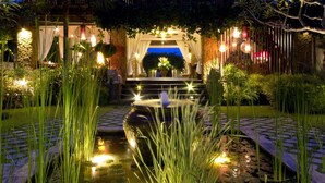 A well-lit outdoor garden with a pond, steps leading to a covered area, and a wooden fence. - 5 Bedroom villa Beachfront with private Pool in Canggu (Canggu)
