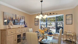 A dining area with a glass-top table, white chairs, and a gold cart.