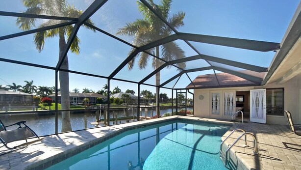 An indoor swimming pool with a glass enclosure, surrounded by palm trees and a view of a residential area.
