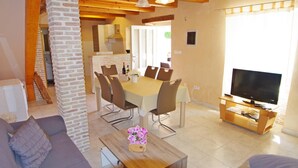 A modern living room with a wooden dining table, chairs, a sofa, a TV, and a fireplace. - Elegant Holiday House in Village Kavran  (Kavran)