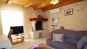 A living room with a fireplace, a television, a sofa, and a wooden coffee table with flowers. - Elegant Holiday House in Village Kavran  (Kavran)