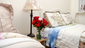 A bedroom with a bed, a nightstand, a lamp, and a vase with red flowers.