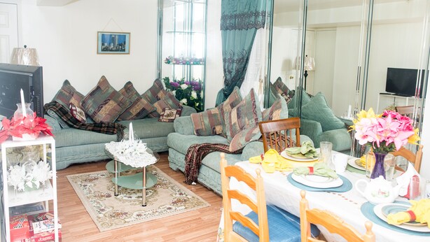A living room with a sofa, a dining table set for two, and a television in the background.