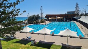 Une grande piscine extérieure dotée de plusieurs couloirs de nage, entourée de chaises longues et de parasols.