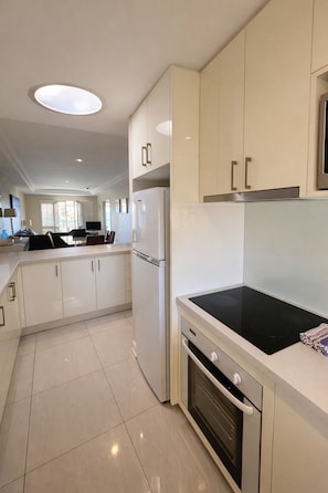 A modern kitchen with white cabinets, a built-in oven, and a black stovetop. - The White Pearl Penthouse (Scarborough)