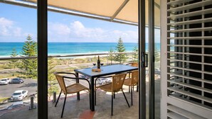 Un balcon avec une table et des chaises, donnant sur une plage et l’océan.