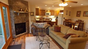 A living room with a stone fireplace, a sofa, a glass coffee table, and a dining area in the background. - Sisters Treehouse (Oakland)