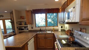 A kitchen with wooden cabinets, a stainless steel sink, a white stove, and a window with a view of trees. - Sisters Treehouse (Oakland)