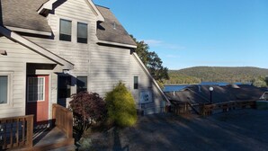 A two-story house with a sloped roof, a front porch with wooden railings, and a view of a lake and hills in the background. - Sisters Treehouse (Oakland)