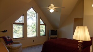 A bedroom with a bed, a TV, a lamp, a ceiling fan, and large windows. - Sisters Treehouse (Oakland)