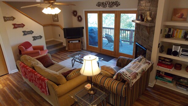 A living room with a sofa, armchair, and a glass coffee table. There's a television on a stand and a fireplace with bookshelves. - Sisters Treehouse (Oakland)