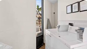 A laundry room with a washing machine, dryer, and a window with a view of palm trees. - OF Condo Gone2TheBeach @ Symphony Beach Club (Ormond Beach)