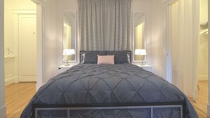 Une chambre avec un grand lit, une table de chevet avec une lampe et un miroir au mur.
