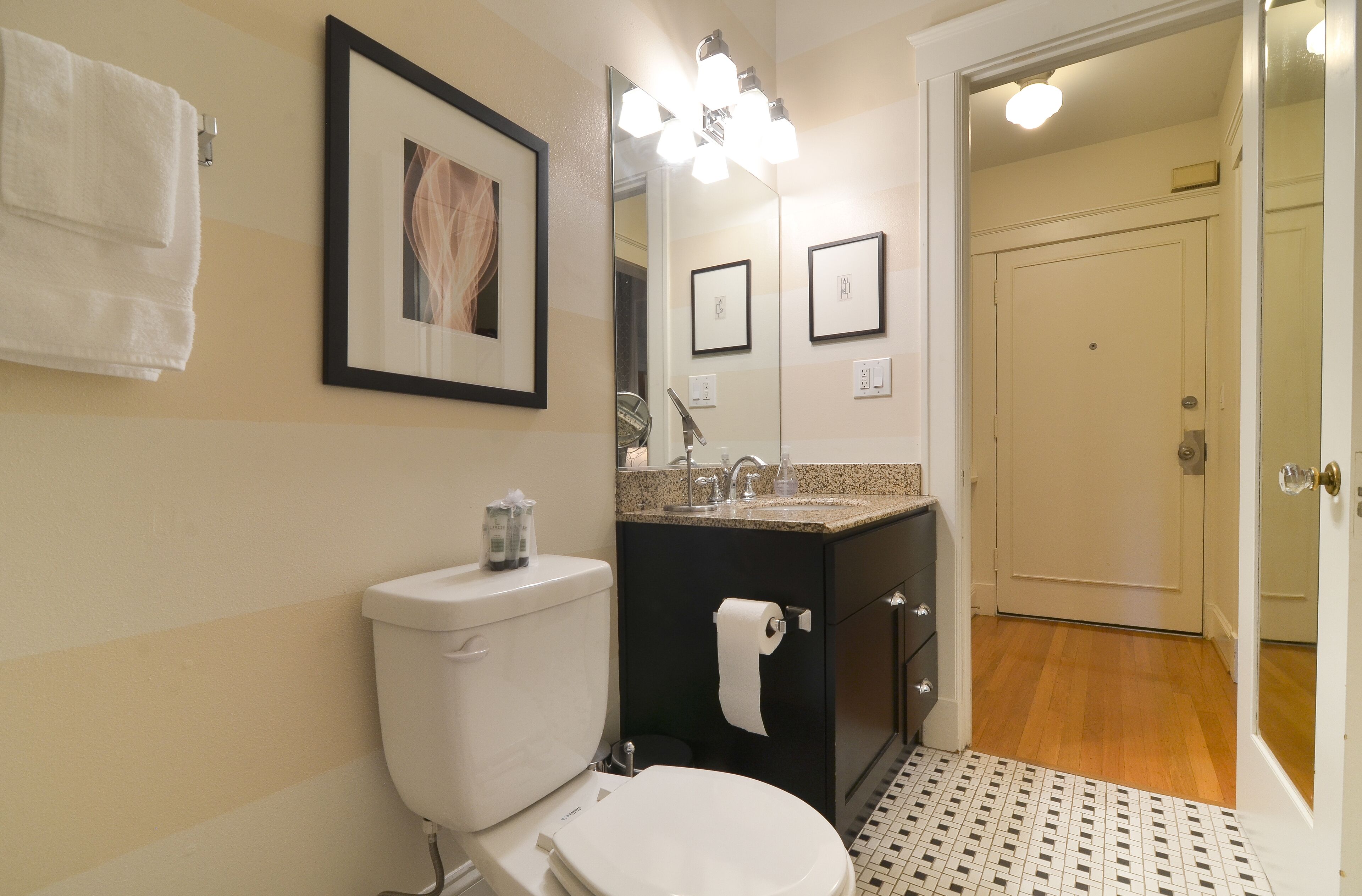 Ein Badezimmer mit Toilette, Waschbecken und Spiegel. Handtücher hängen an der Wand und ein gerahmtes Bild ist über dem Spiegel.