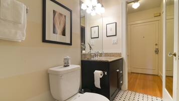 Ein Badezimmer mit Toilette, Waschbecken und Spiegel. Handtücher hängen an der Wand und ein gerahmtes Bild ist über dem Spiegel.