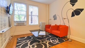 Un salon moderne avec une table basse en verre, un canapé rouge, une lampe sur pied et un téléviseur fixé au mur.