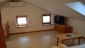 Ein kleiner, gemütlicher Wohnraum mit Holzboden, zwei Fenstern, einem Fernseher und einem Holztisch.