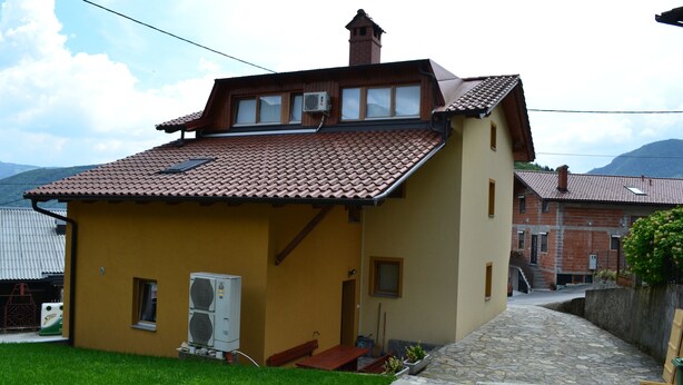 Ein kleines, gelbes Gebäude mit einem Ziegeldach, einem Schornstein und einer kleinen Veranda mit einer Bank.
