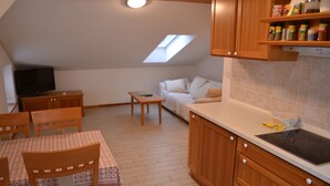 Eine gemütliche Küche mit Holzschränken, einem Esstisch mit Stühlen, einem kleinen Couchtisch und einem Fernseher in der Ecke.