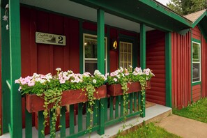 A red wooden cottage with a green porch, a number sign, and flower boxes.