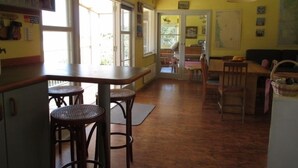 A kitchen with a bar area, wooden flooring, and a dining table with chairs. - Simply the best! Beach front, uninterrupted great views from all rooms (Whiritoa)