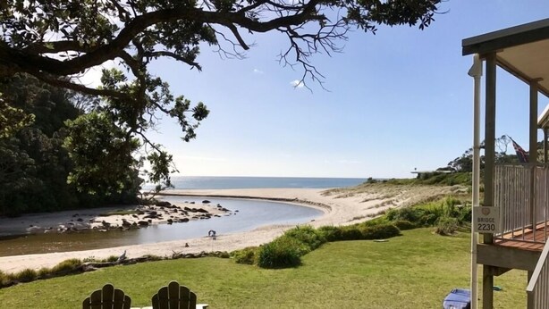 A view of a beach with two Adirondack chairs facing the ocean, a wooden deck, and a sign indicating 'Bridge 2230'. - Simply the best! Beach front, uninterrupted great views from all rooms (Whiritoa)
