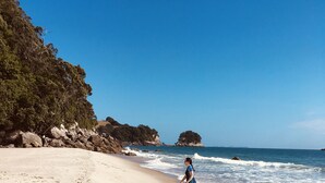 A sandy beach with footprints, a child playing, and a person walking in the background. - Simply the best! Beach front, uninterrupted great views from all rooms (Whiritoa)