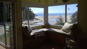 A room with a large bay window overlooking a beach, a cushioned bench, and a chair. - Simply the best! Beach front, uninterrupted great views from all rooms (Whiritoa)