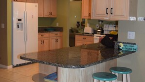 A kitchen with wooden cabinets, a built-in island with stools, a refrigerator, and a sink. - Waterfront Vacation home, Private Pool, Lanai, Dock, Walk to Beach (Marco Island)