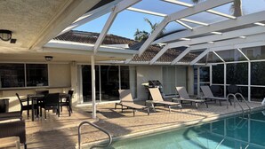 A poolside area with lounge chairs, a barbecue grill, and a covered patio. - Waterfront Vacation home, Private Pool, Lanai, Dock, Walk to Beach (Marco Island)