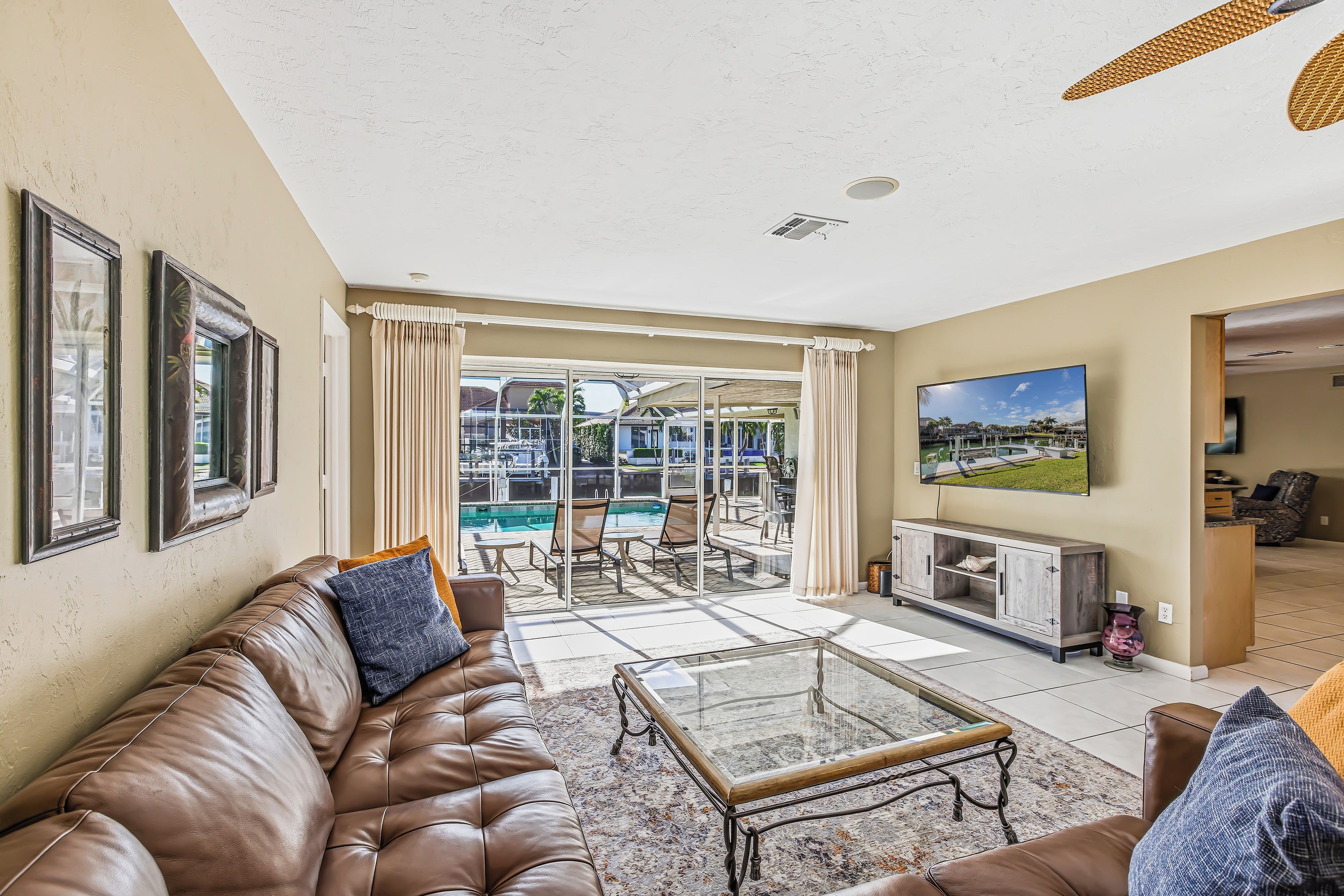 A spacious living room with a leather sofa, a glass coffee table, and a view of a pool area through large windows.