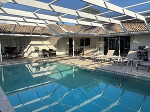 Un área de piscina con sillones de descanso, una parrilla y un porche cubierto.