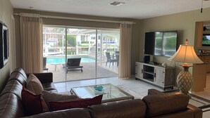 A living room with a leather sofa, a glass coffee table, a flat-screen TV, and a ceiling fan. - Waterfront Vacation home, Private Pool, Lanai, Dock, Walk to Beach (Marco Island)
