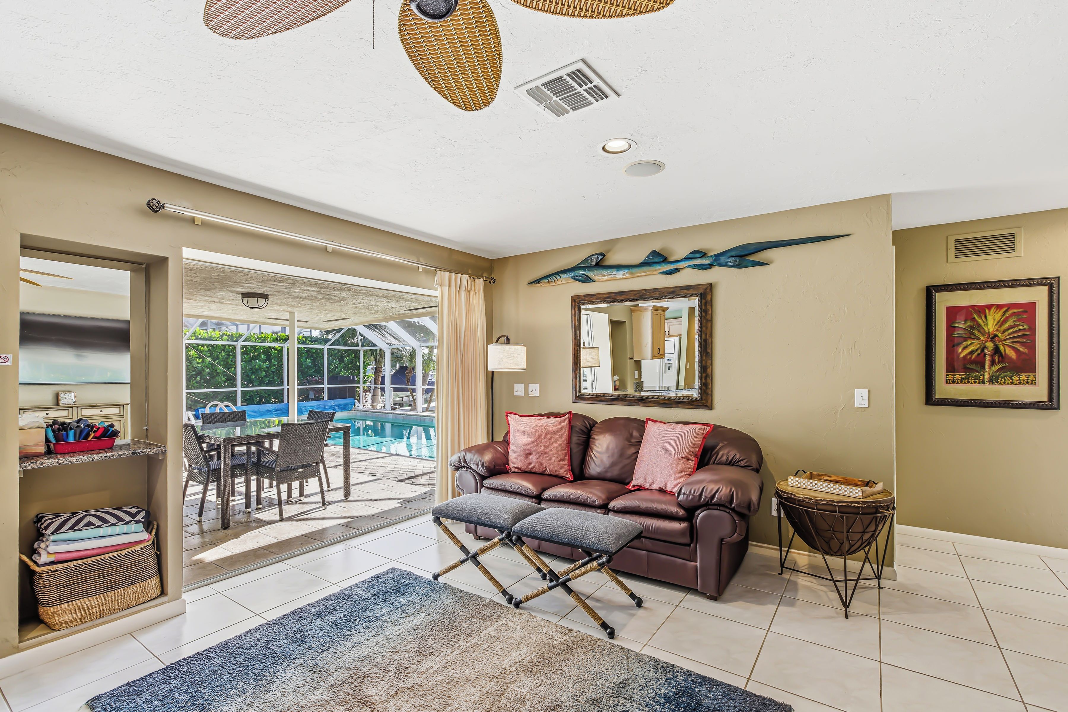 A living room with a leather sofa, a glass coffee table, a patterned rug, and a view of an outdoor swimming pool.