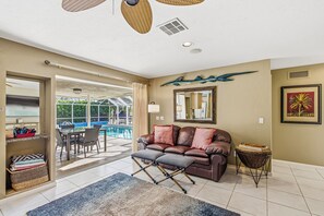 A living room with a leather sofa, a glass coffee table, a patterned rug, and a view of an outdoor swimming pool.